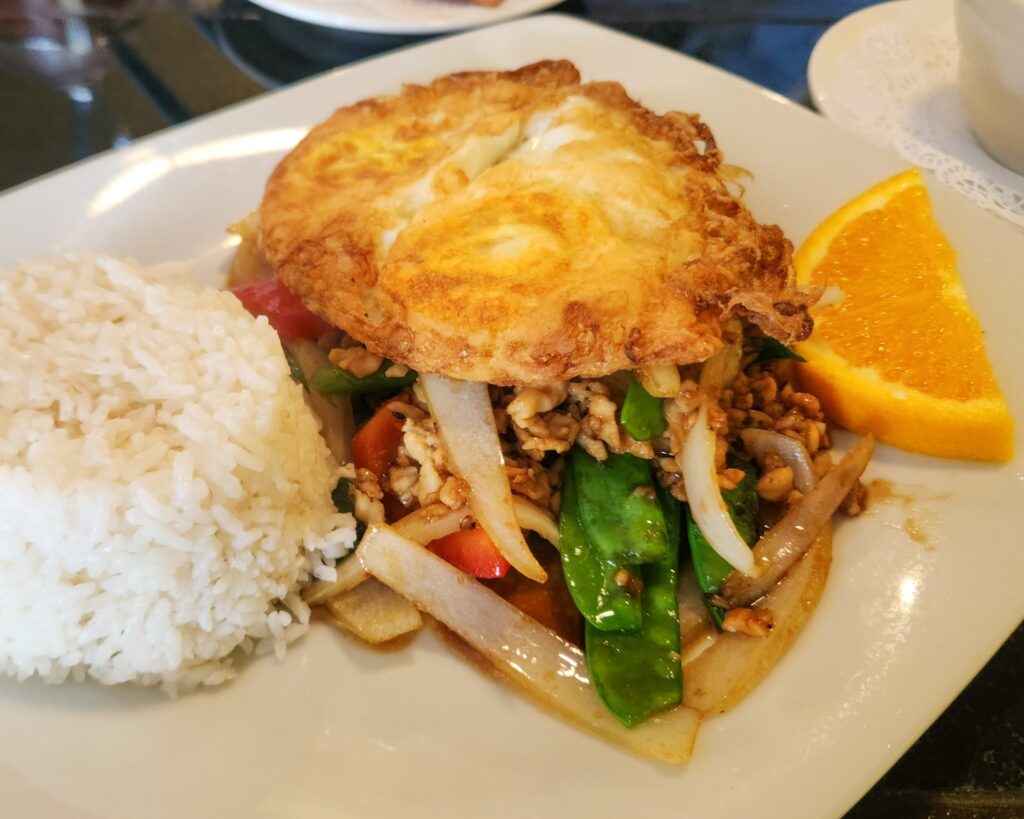 a bowl of minced chicken with Thai basil atop jasmine rice, topped with a fried egg